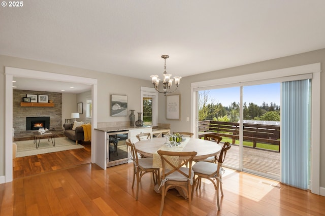 dining space featuring an inviting chandelier, a fireplace, light wood-style floors, wine cooler, and visible vents