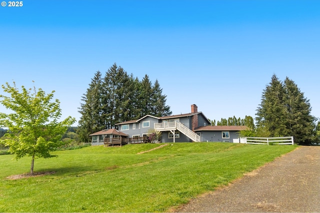 view of front of house featuring fence, a front yard, a deck, a chimney, and stairs