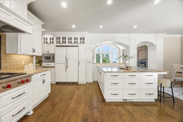 kitchen featuring a breakfast bar, light stone counters, arched walkways, dark wood finished floors, and appliances with stainless steel finishes