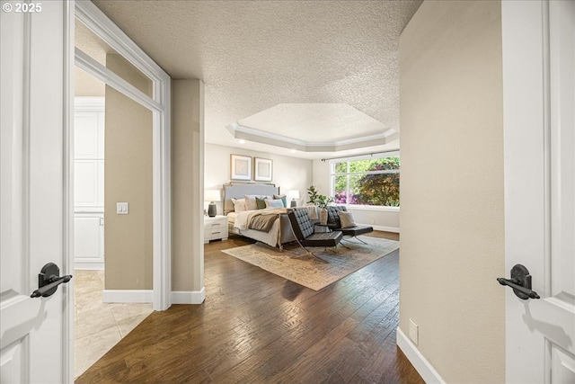bedroom featuring a textured ceiling, hardwood / wood-style flooring, baseboards, and a raised ceiling