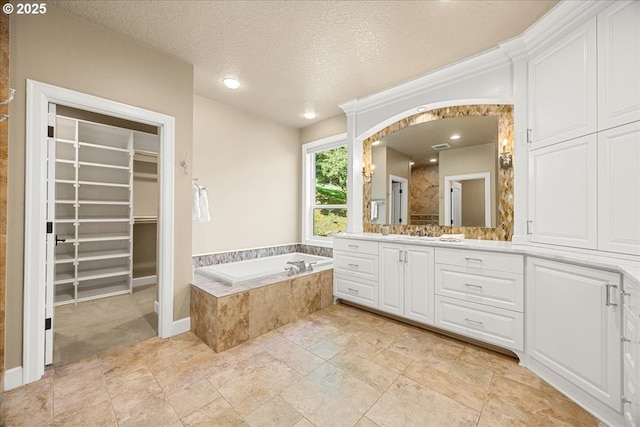 full bathroom featuring a walk in closet, a garden tub, a textured ceiling, vanity, and tiled shower
