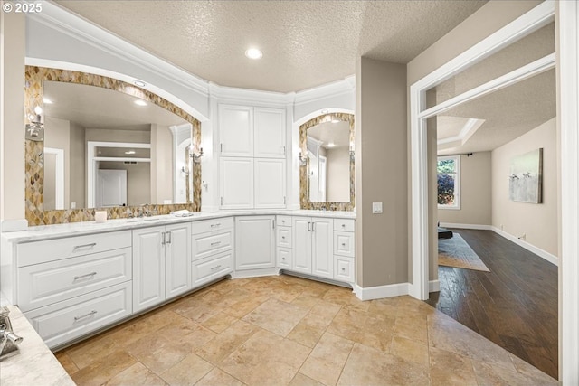full bathroom featuring double vanity, baseboards, ornamental molding, and a textured ceiling