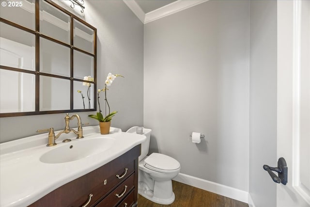 half bath with crown molding, wood finished floors, vanity, baseboards, and toilet