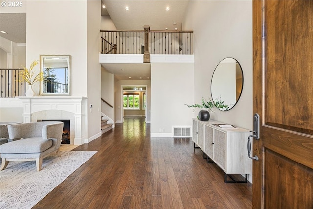 foyer featuring dark wood-style flooring, visible vents, a towering ceiling, stairway, and baseboards
