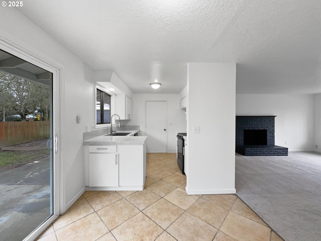 kitchen with sink, a textured ceiling, light carpet, a fireplace, and white cabinets