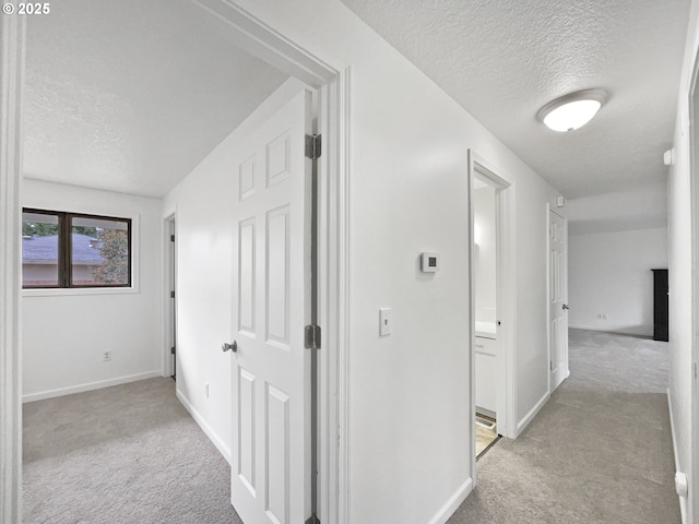 corridor with light carpet and a textured ceiling