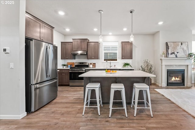 kitchen featuring dark brown cabinetry, appliances with stainless steel finishes, a sink, a kitchen breakfast bar, and under cabinet range hood