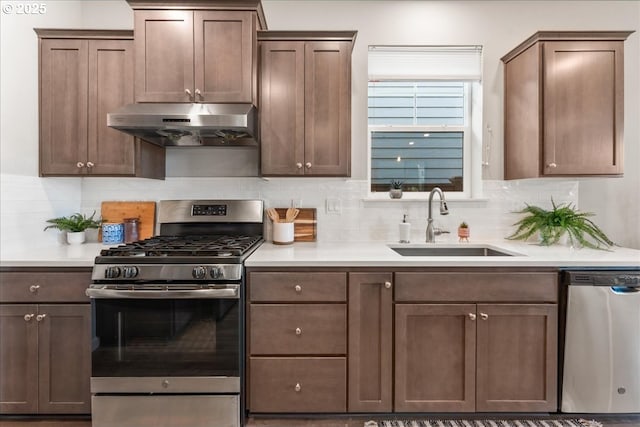 kitchen with appliances with stainless steel finishes, a sink, light countertops, backsplash, and under cabinet range hood