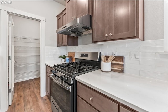 kitchen featuring gas range, tasteful backsplash, wood finished floors, light countertops, and under cabinet range hood