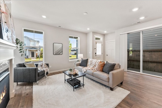 living room with a glass covered fireplace, recessed lighting, and wood finished floors