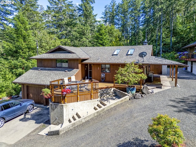 view of front of home with roof with shingles, driveway, a chimney, and a wooden deck