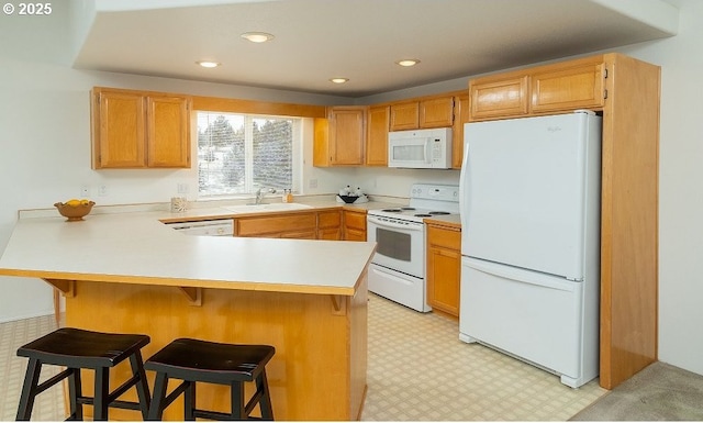 kitchen featuring white appliances, a breakfast bar, kitchen peninsula, and sink