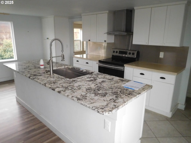 kitchen featuring a kitchen island with sink, wall chimney range hood, white cabinetry, and stainless steel electric stove