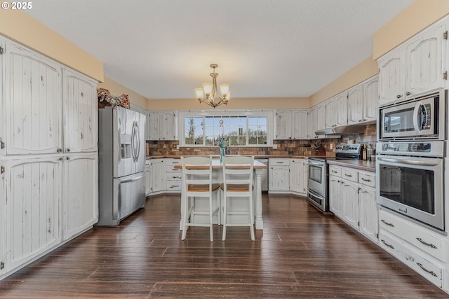 kitchen with appliances with stainless steel finishes, an inviting chandelier, a center island, dark hardwood / wood-style flooring, and decorative backsplash