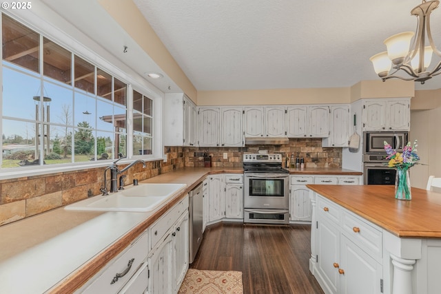 kitchen with sink, white cabinetry, backsplash, stainless steel appliances, and decorative light fixtures