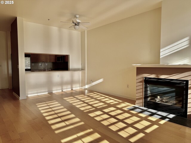 821 NW 11th Ave Unit 315, Portland, OR 97209 - unfurnished living room featuring a fireplace with flush hearth, wood finished floors, ceiling fan, a sink, and baseboards