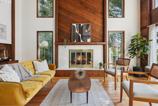 living room featuring a glass covered fireplace, wood finished floors, a high ceiling, and wooden walls