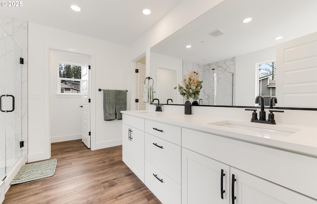 bathroom featuring a marble finish shower, double vanity, recessed lighting, wood finished floors, and a sink