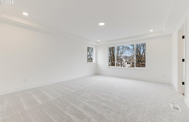 unfurnished room featuring a tray ceiling, visible vents, light colored carpet, and recessed lighting