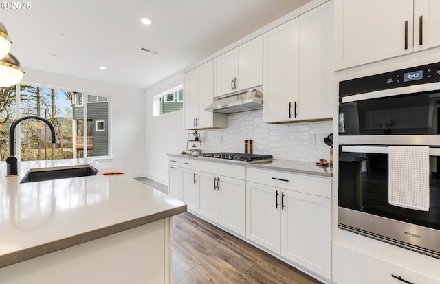 kitchen featuring double wall oven, a sink, decorative backsplash, stainless steel gas stovetop, and under cabinet range hood