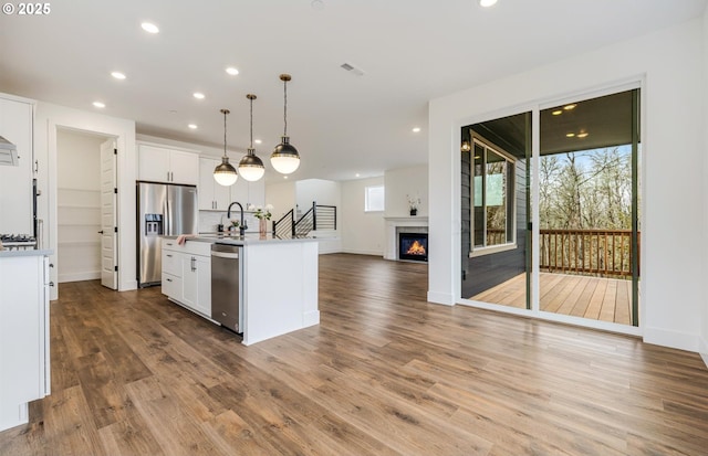 kitchen with open floor plan, white cabinets, stainless steel appliances, and a glass covered fireplace