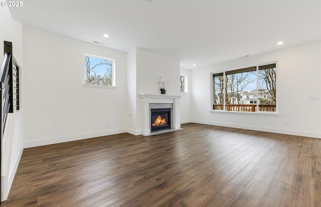 unfurnished living room featuring dark wood-style floors, visible vents, a fireplace, and a wealth of natural light