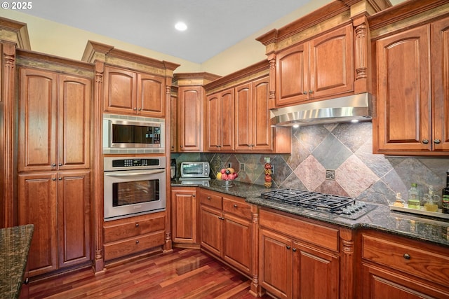 6147 Quail Hollow St, Salem, OR 97306 - kitchen featuring stainless steel appliances, under cabinet range hood, dark stone counters, decorative backsplash, and brown cabinets