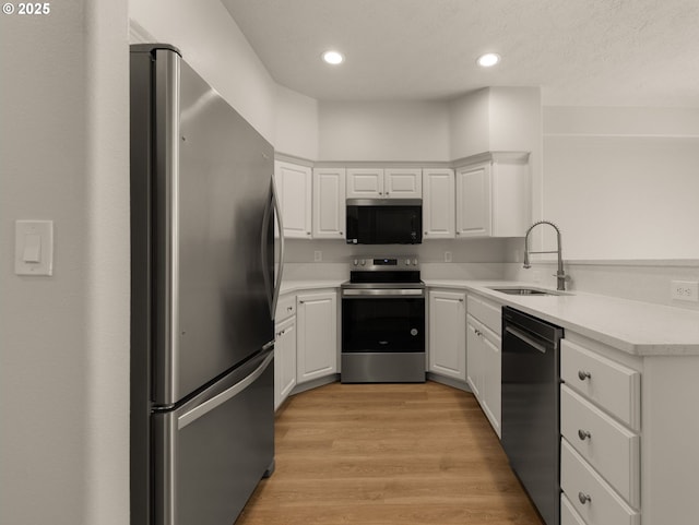 kitchen with a sink, appliances with stainless steel finishes, white cabinetry, light countertops, and recessed lighting