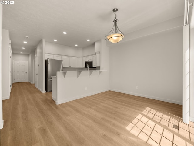 kitchen featuring freestanding refrigerator, white cabinetry, a peninsula, light wood-style flooring, and recessed lighting