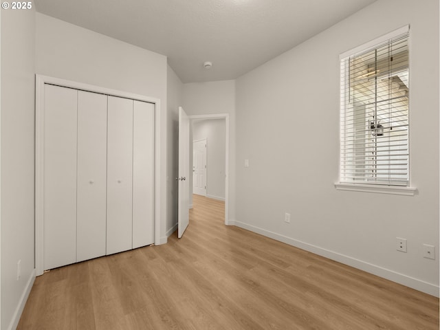unfurnished bedroom with baseboards, light wood finished floors, and a closet