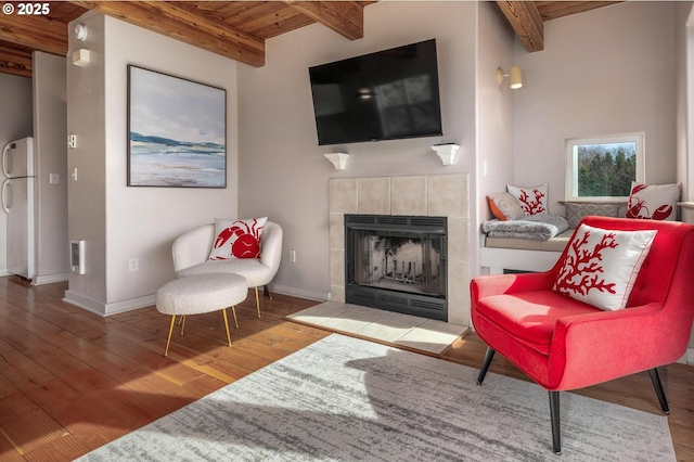 living area featuring wood ceiling, a tile fireplace, beam ceiling, and wood finished floors