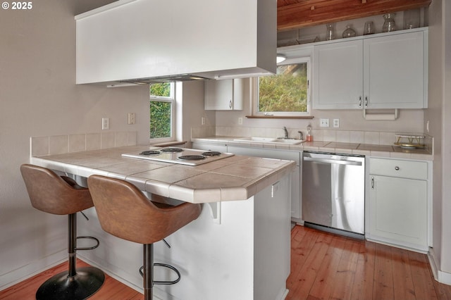 kitchen featuring dishwasher, tile countertops, white cooktop, range hood, and a sink