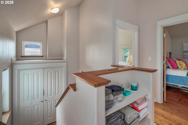 hallway featuring an upstairs landing, vaulted ceiling, and light wood finished floors