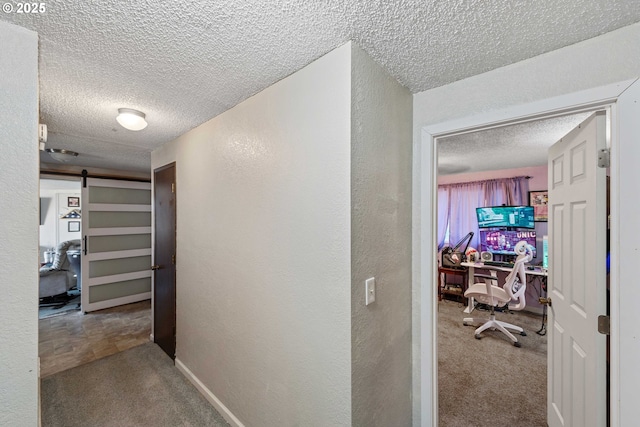 hallway with a barn door, a textured ceiling, and carpet