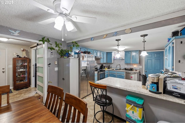 kitchen with sink, kitchen peninsula, stainless steel appliances, a barn door, and blue cabinetry