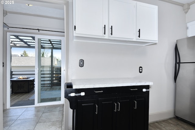 kitchen with freestanding refrigerator, dark cabinetry, light countertops, white cabinetry, and baseboards