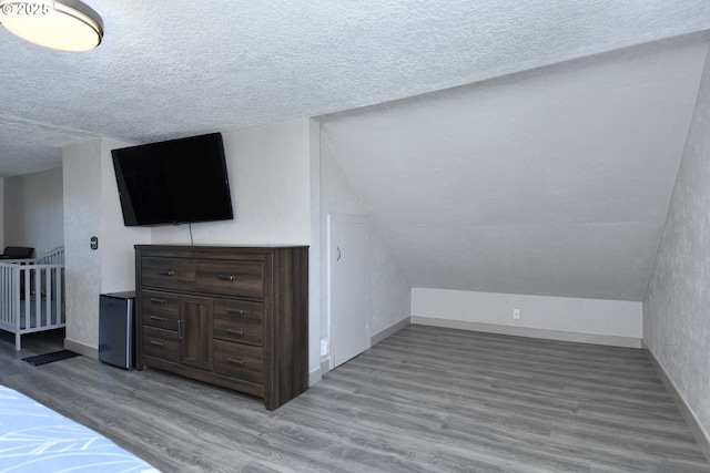 unfurnished bedroom featuring a textured ceiling, wood finished floors, baseboards, and lofted ceiling