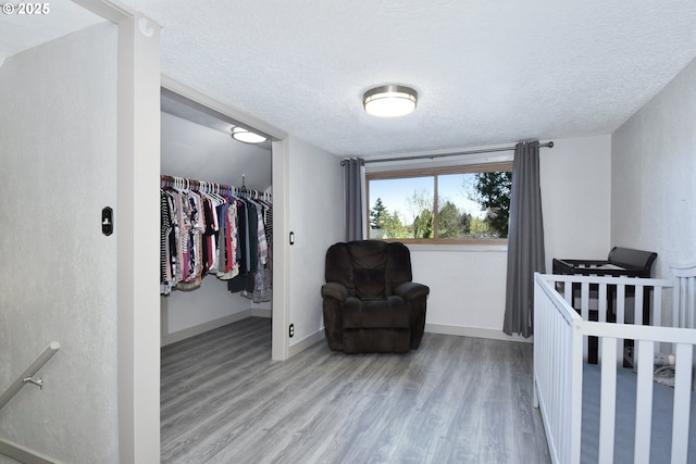 bedroom featuring a textured ceiling, wood finished floors, baseboards, a closet, and a spacious closet