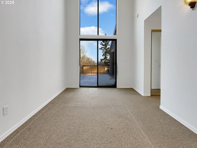 spare room with carpet flooring, a towering ceiling, and baseboards