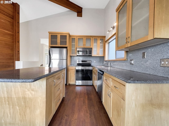 kitchen featuring tasteful backsplash, dark stone counters, lofted ceiling with beams, stainless steel appliances, and a sink