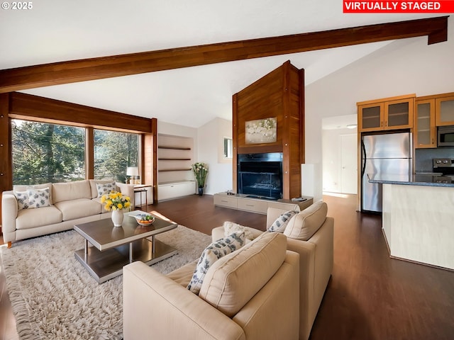 living area featuring lofted ceiling with beams, dark wood finished floors, and a glass covered fireplace