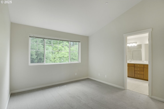 unfurnished bedroom featuring light carpet, baseboards, vaulted ceiling, ensuite bathroom, and a sink