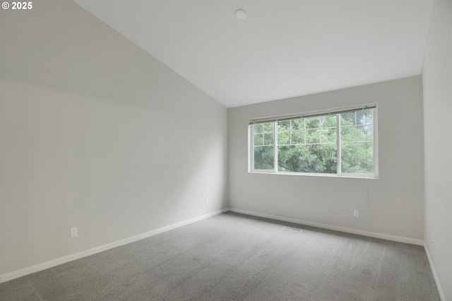 carpeted spare room featuring lofted ceiling and baseboards