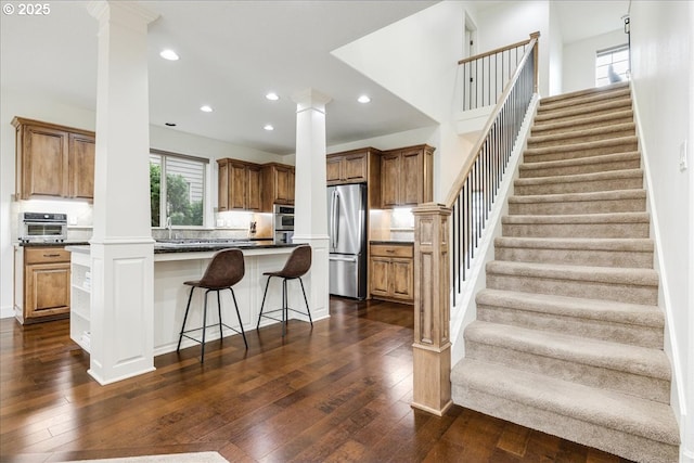 kitchen with stainless steel appliances, dark wood-type flooring, decorative columns, and a kitchen breakfast bar