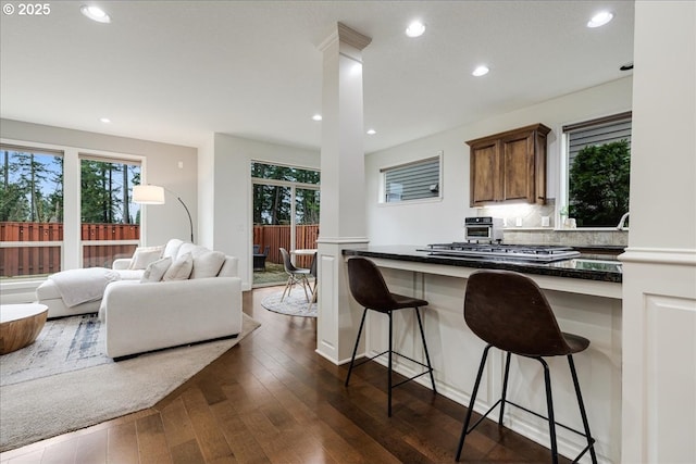 kitchen with a breakfast bar, dark wood finished floors, stainless steel gas cooktop, decorative columns, and open floor plan