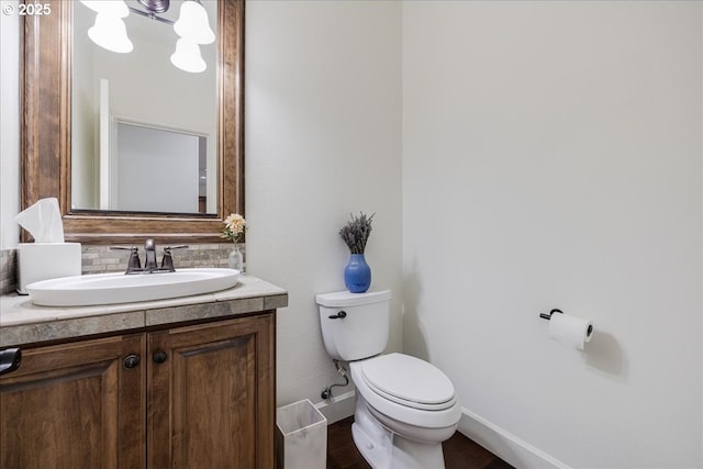 half bathroom with toilet, wood finished floors, vanity, baseboards, and decorative backsplash