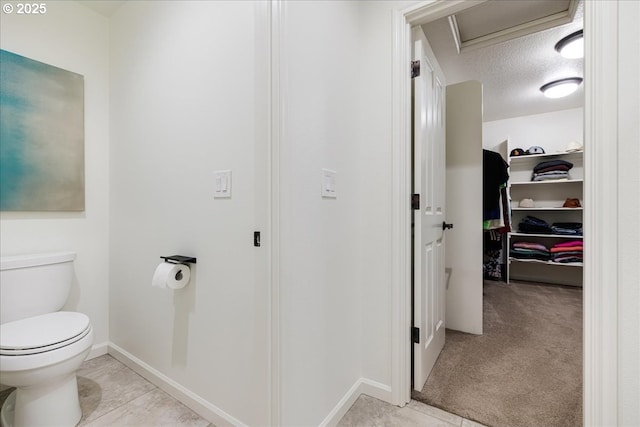 bathroom with a textured ceiling, toilet, baseboards, a closet, and tile patterned floors