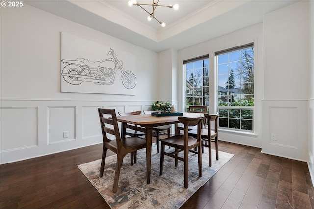 dining area with dark wood finished floors, a raised ceiling, a decorative wall, and an inviting chandelier