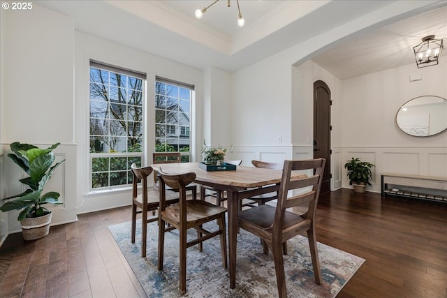 dining room featuring arched walkways, a wainscoted wall, a raised ceiling, an inviting chandelier, and dark wood-type flooring