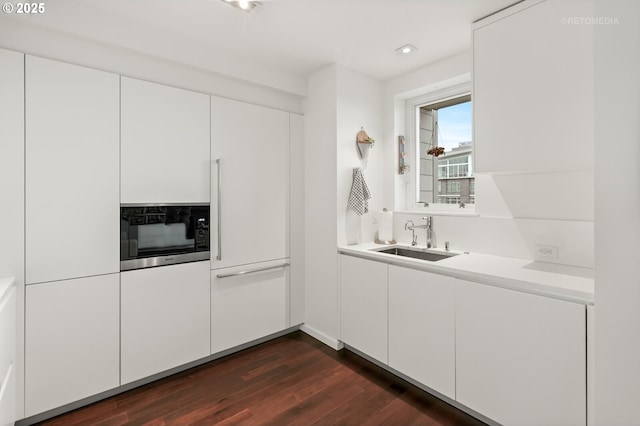 kitchen with black microwave, dark wood-style floors, light countertops, white cabinetry, and a sink